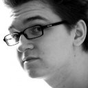 Black and white image of a male face in profile wearing glasses with a thick black frame